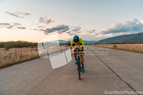 Image of Triathlete riding his bicycle during sunset, preparing for a marathon. The warm colors of the sky provide a beautiful backdrop for his determined and focused effort.