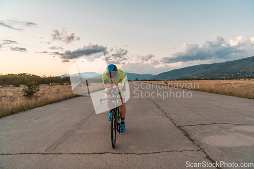 Image of Triathlete riding his bicycle during sunset, preparing for a marathon. The warm colors of the sky provide a beautiful backdrop for his determined and focused effort.