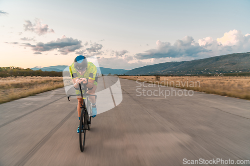 Image of Triathlete riding his bicycle during sunset, preparing for a marathon. The warm colors of the sky provide a beautiful backdrop for his determined and focused effort.