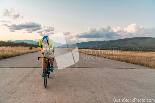 Image of Triathlete riding his bicycle during sunset, preparing for a marathon. The warm colors of the sky provide a beautiful backdrop for his determined and focused effort.