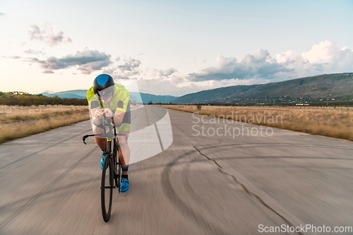 Image of Triathlete riding his bicycle during sunset, preparing for a marathon. The warm colors of the sky provide a beautiful backdrop for his determined and focused effort.