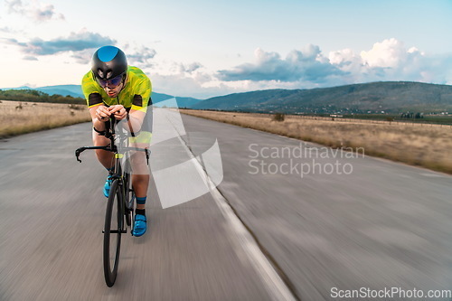 Image of Triathlete riding his bicycle during sunset, preparing for a marathon. The warm colors of the sky provide a beautiful backdrop for his determined and focused effort.