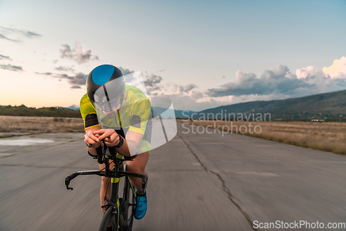 Image of Triathlete riding his bicycle during sunset, preparing for a marathon. The warm colors of the sky provide a beautiful backdrop for his determined and focused effort.