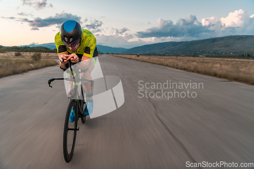 Image of Triathlete riding his bicycle during sunset, preparing for a marathon. The warm colors of the sky provide a beautiful backdrop for his determined and focused effort.