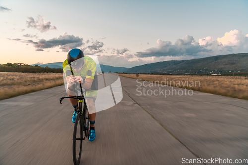 Image of Triathlete riding his bicycle during sunset, preparing for a marathon. The warm colors of the sky provide a beautiful backdrop for his determined and focused effort.