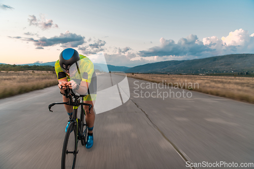 Image of Triathlete riding his bicycle during sunset, preparing for a marathon. The warm colors of the sky provide a beautiful backdrop for his determined and focused effort.