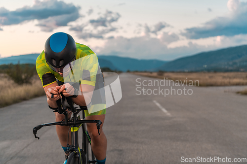 Image of Triathlete riding his bicycle during sunset, preparing for a marathon. The warm colors of the sky provide a beautiful backdrop for his determined and focused effort.