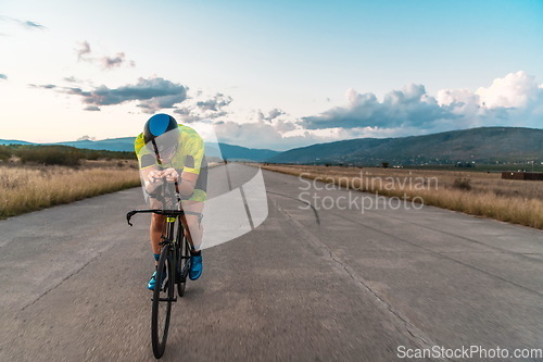 Image of Triathlete riding his bicycle during sunset, preparing for a marathon. The warm colors of the sky provide a beautiful backdrop for his determined and focused effort.