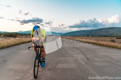 Image of Triathlete riding his bicycle during sunset, preparing for a marathon. The warm colors of the sky provide a beautiful backdrop for his determined and focused effort.