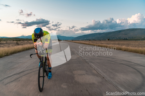 Image of Triathlete riding his bicycle during sunset, preparing for a marathon. The warm colors of the sky provide a beautiful backdrop for his determined and focused effort.