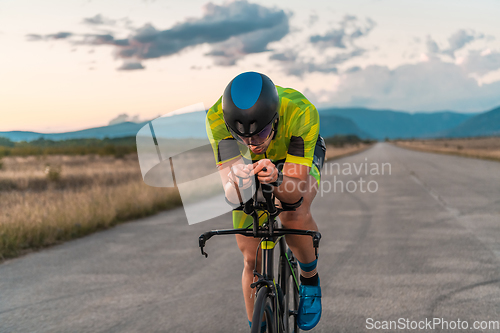 Image of Triathlete riding his bicycle during sunset, preparing for a marathon. The warm colors of the sky provide a beautiful backdrop for his determined and focused effort.