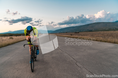 Image of Triathlete riding his bicycle during sunset, preparing for a marathon. The warm colors of the sky provide a beautiful backdrop for his determined and focused effort.