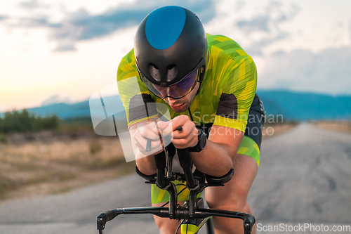 Image of Close up photo of triathlete riding his bicycle during sunset, preparing for a marathon. The warm colors of the sky provide a beautiful backdrop for his determined and focused effort.