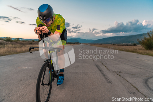 Image of Triathlete riding his bicycle during sunset, preparing for a marathon. The warm colors of the sky provide a beautiful backdrop for his determined and focused effort.