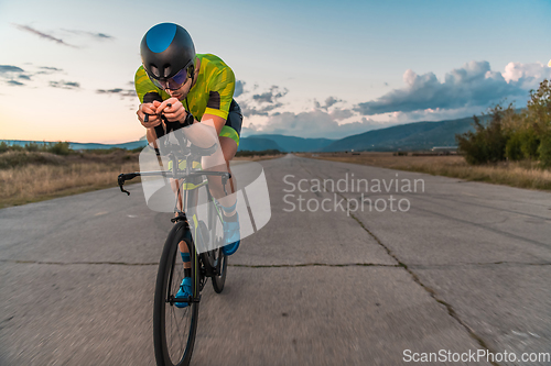 Image of Triathlete riding his bicycle during sunset, preparing for a marathon. The warm colors of the sky provide a beautiful backdrop for his determined and focused effort.