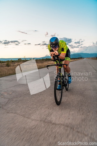 Image of Triathlete riding his bicycle during sunset, preparing for a marathon. The warm colors of the sky provide a beautiful backdrop for his determined and focused effort.