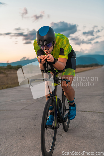 Image of Triathlete riding his bicycle during sunset, preparing for a marathon. The warm colors of the sky provide a beautiful backdrop for his determined and focused effort.