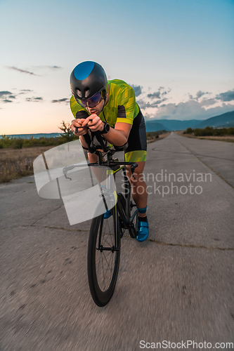 Image of Triathlete riding his bicycle during sunset, preparing for a marathon. The warm colors of the sky provide a beautiful backdrop for his determined and focused effort.