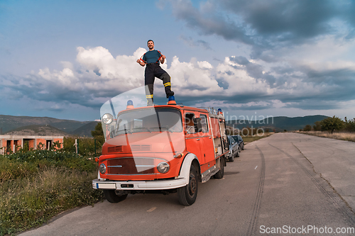 Image of The firefighter standing confidently on the fire truck, ready to respond to any emergency.