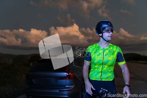 Image of A triathlete resting on the road after a tough bike ride in the dark night, leaning on his bike in complete exhaustion