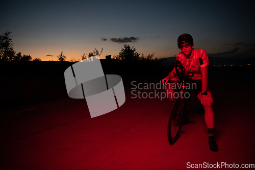 Image of A triathlete resting on the road after a tough bike ride in the dark night, leaning on his bike in complete exhaustion