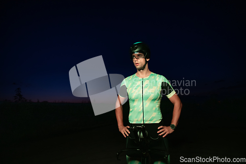Image of A triathlete resting on the road after a tough bike ride in the dark night, leaning on his bike in complete exhaustion