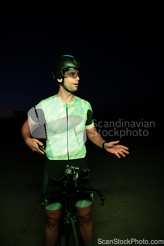 Image of A triathlete resting on the road after a tough bike ride in the dark night, leaning on his bike in complete exhaustion