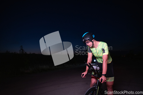 Image of A triathlete resting on the road after a tough bike ride in the dark night, leaning on his bike in complete exhaustion