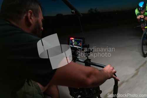 Image of A videographer recording a triathlete riding his bike preparing for an upcoming marathon.Athlete's physical endurance and the dedication required to succeed in the sport.