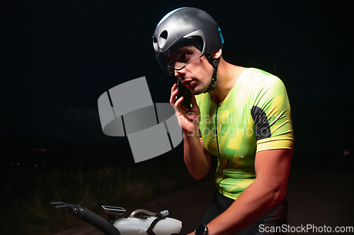 Image of A triathlete using a smartphone while taking a break from a hard night's cycling training