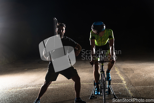 Image of Behind the scenes. Professional videographer on a night shoot with a triathlete riding a bicycle for video recording purposes