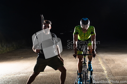 Image of Behind the scenes. Professional videographer on a night shoot with a triathlete riding a bicycle for video recording purposes