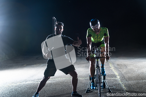 Image of Behind the scenes. Professional videographer on a night shoot with a triathlete riding a bicycle for video recording purposes