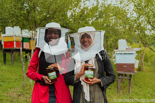 Image of Portrait of an Arab investors holding a jar of honey in their hands while standing in front of a large honey farm. The concept of investing in small businesses