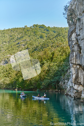 Image of A group of friends enjoying having fun and kayaking while exploring the calm river, surrounding forest and large natural river canyons