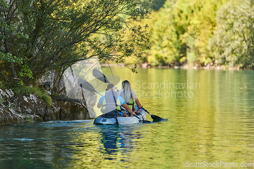 Image of A young couple enjoying an idyllic kayak ride in the middle of a beautiful river surrounded by forest greenery