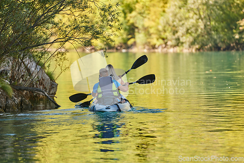 Image of A young couple enjoying an idyllic kayak ride in the middle of a beautiful river surrounded by forest greenery