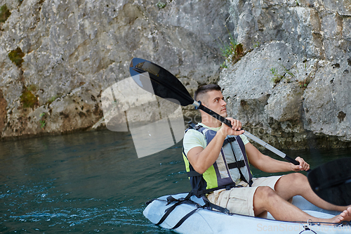 Image of A young man kayaking and exploring a river, surrounded by an impressive natural scenery that exudes an adventurous spirit