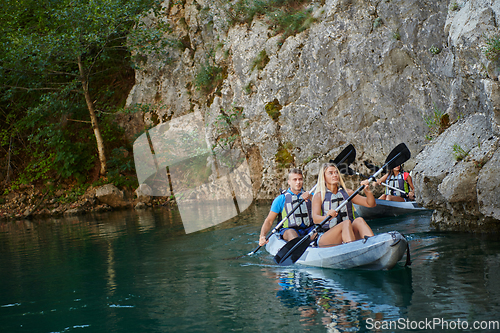 Image of A group of friends enjoying having fun and kayaking while exploring the calm river, surrounding forest and large natural river canyons