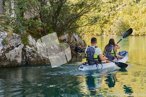 Image of A young couple enjoying an idyllic kayak ride in the middle of a beautiful river surrounded by forest greenery