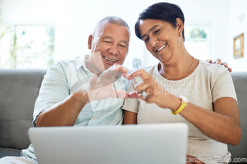 Image of Mature couple, heart hands and laptop on home sofa for video call, streaming and internet. A happy man and woman together on a couch with technology for communication, social media emoji or love