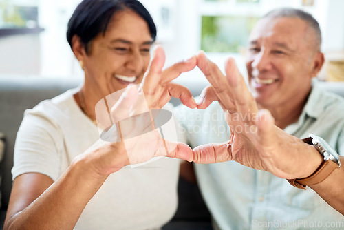 Image of Mature couple, heart hands and love on home sofa for connection, marriage and bond. A happy man and woman together on a couch with emoji, shape or symbol for commitment, trust or health and wellness