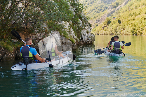 Image of A group of friends enjoying having fun and kayaking while exploring the calm river, surrounding forest and large natural river canyons