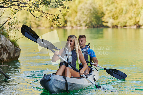 Image of A young couple enjoying an idyllic kayak ride in the middle of a beautiful river surrounded by forest greenery