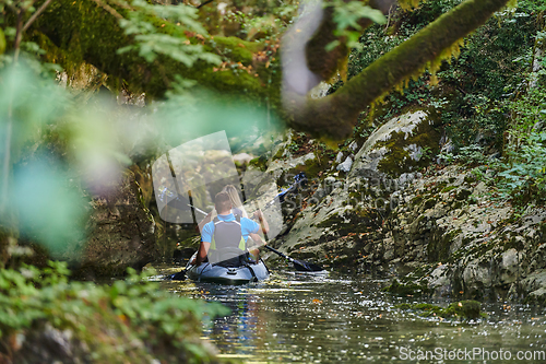 Image of A young couple enjoying an idyllic kayak ride in the middle of a beautiful river surrounded by forest greenery