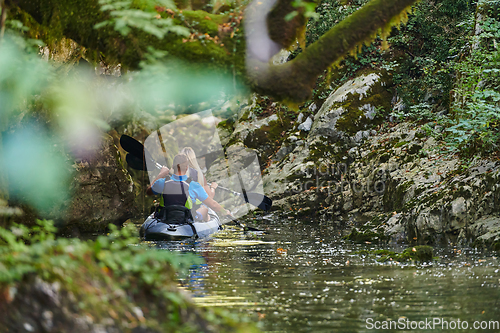 Image of A young couple enjoying an idyllic kayak ride in the middle of a beautiful river surrounded by forest greenery