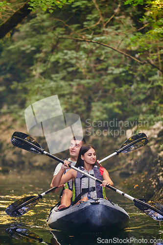 Image of A young couple enjoying an idyllic kayak ride in the middle of a beautiful river surrounded by forest greenery