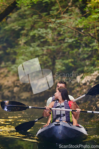 Image of A young couple enjoying an idyllic kayak ride in the middle of a beautiful river surrounded by forest greenery