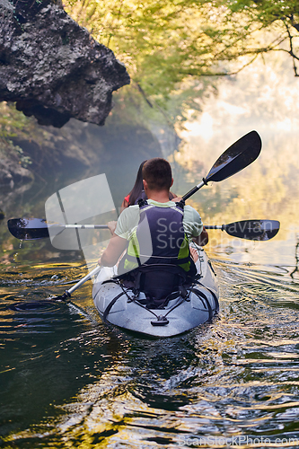 Image of A young couple enjoying an idyllic kayak ride in the middle of a beautiful river surrounded by forest greenery