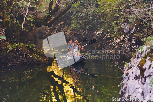 Image of A young couple enjoying an idyllic kayak ride in the middle of a beautiful river surrounded by forest greenery